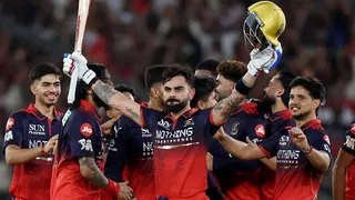 Virat Kohli holds his bat and helmet aloft as his RCB team-mates celebrate winning the IPL