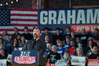 man stands at podium marked 'fight oligarchy' at rally