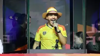 Getty Images Abelardo de la Espriella speaks behind bulletproof glass during a campaign rally in Medellin. He wears a Colombia football shirt and striped hat.