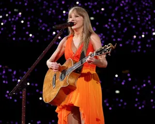 Woman in orange dress singing on stage while playing guitar