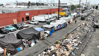 A person walking past large piles of trash inside a homeless encampment in downtown Los Angeles