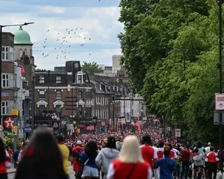 A large crowd fills a street lined with shops and trees, many wearing red and white