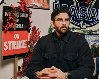 Hasan Piker sits with hands clasped in front of strike signs and holiday decorations