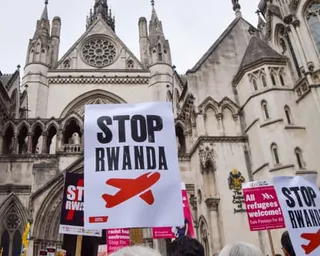 People holding up signs reading: 'Stop Rwanda' and 'All refugees welcome' in front of the building.