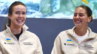 Elina Svitolina and Marta Kostyuk sit together and smile wearing cream zip-up jackets