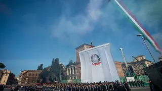 armed forces in front of massive flag and below air show