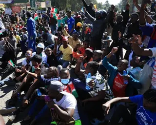 A crowd of protesters sitting on the ground with their arms in the air
