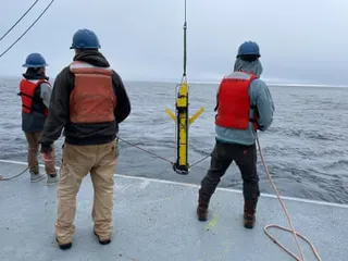 Three people in hard hats and life jackets deploy a yellow glider from a boat deck