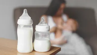 Mother breastfeeding baby while holding the child in her hands with bottles of breast milk in the background