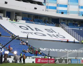 A large white banner reading "OLA SI, GRITO NO" is displayed across blue stadium seating