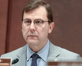 A man in glasses and suit and tie sits and listens
