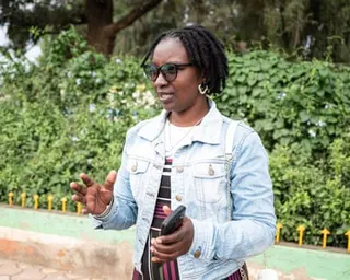 Kendi is wearing a denim jacket and holding her phone as she speaks to someone off-camera