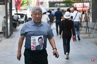 韩国第九届地方选举最大焦点是首尔市长选举。作为韩国人口最多、政治影响力最大的地区，首尔历来被视为全国政治风向标，其结果往往被解读为民意走向的重要指标。图为一名男子胸前贴上首尔市长候选人郑愿伍的竞选海报四处奔走拉票。 （法新社）