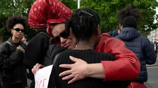 A woman in red  wearing glasses upset hugging a woman in a black jumper.