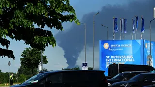 Cars are seen parked near banners with branding for the St. Petersburg International Economic Forum (SPIEF) at the forum's venue as black smoke rises in distance in Saint Petersburg on June 3, 2026.