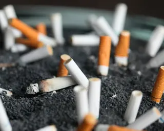Multiple cigarette butts with orange filters are stubbed out in a black ashtray