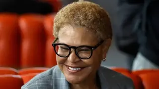 Getty Images This is a head and shoulders pic of Karen Bass who is smiling broadly and wearing a grey, checked suit. The background, slightly out of focus, appears to be red seating