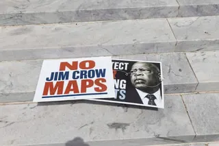 Protest signs reading 'NO JIM CROW MAPS' lie on Alabama state capitol steps with a photo of a person