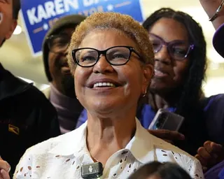 Los Angeles Mayor Karen Bass in glasses and a white eyelet shirt stands among a group at an indoor event
