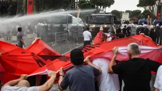 Reuters Water cannons are fired at a row of protesters holding Albanian flags from two large police vehicles in a city square.