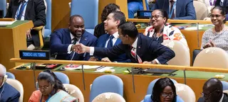 特立尼达和多巴哥代表在United Nations安理会会议上庆祝胜利，在会议厅内握手。