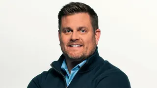 Brian Thompson smiling in a blue button down shirt and blue zip-up jacket