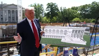 Trump stands outside the construction site of the ballroom, gesturing while holding a rendering of what the finished building will look like, with trees in the background on a sunny day in Washington DC in May.