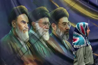 An woman walks past a banner in Tehran bearing portraits of Ayatollah Ruhollah Khomeini, Ali Khamenei and Mojtaba Khamenei.