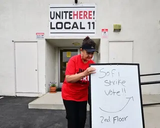 Woman in red shirt moves whiteboard sandwich board outdoors.