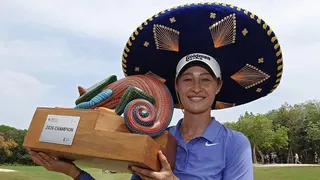 Nelly Korda celebrates winning the Riviera Maya Open in Mexico, wearing a traditional large Mexican hat and blue golf shirt, smiling, and holding a colourful trophy