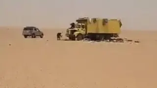 Agadez governorate/Facebook A yellow lorry and a gray SUV are parked in a vast desert landscape, with a few people standing nearby on the open sand