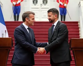 Emmanuel Macron shakes hands with Jakov Milatović next to lecterns and red-carpeted steps