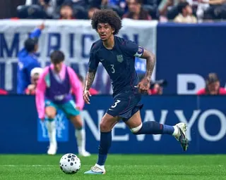 Chris Richards in a dark blue uniform dribbles a ball on a pitch during a match