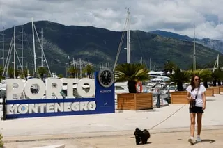 A woman walks her dog next to a marina and sign saying ‘Porto Montenegro’