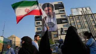 A woman holds up an Iranian flag in front of a banner showing a portrait of the Supreme Leader Ayatollah Mojtaba Khamenei during a street festival celebrating the Muslim Shiite holiday of Eid al-Ghadi