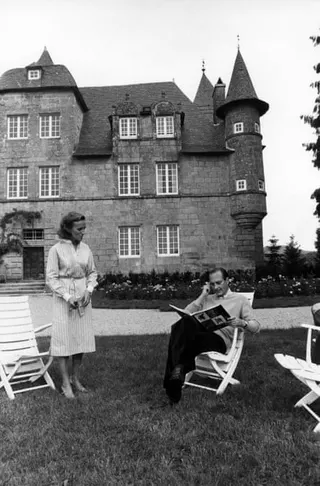 Bernadette Chirac stands next to her husband, who is sitting reading a book, in front of Château de Bity in Sarran