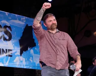 A tattooed, mustachioed man raises his fist