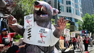 Protesters holding Kick ICE Out signs on an inflatable rat outside SoFi Stadium