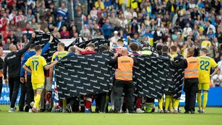 Denmark and Ukraine players forming a ring around Christian Eriksen, as well as security holding large black sheeting.