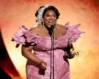 woman in pink dress speaks into microphone while holding trophy on stage