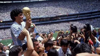 Getty Images The Argentinian captain, Diego Maradona, is held up on the shoulders of fans as he holds the World Cup in his hands and celebrates winning the tournament in 1986 inside a packed stadium. There are people taking pictures of him. In the background we see thousands of people in the stands and a glimpse of the football pitch.