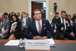 a man adjusts his suit jacket as he sits at a table with people sitting behind him