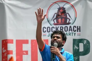 Abhijeet Dipke speaking into a microphone in front of a Coackroach party banner
