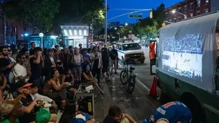 Getty Images dozens of people gather on a pavement to watch a Knicks game projected onto a sheet on a vehicle