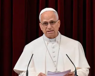 Pope in white makes an address with microphones in front and paper in hand