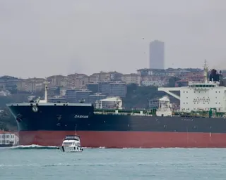 A tanker sails on a river against an urban backdrop