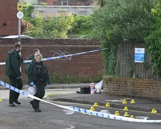 Police officers in green uniforms examine a cordoned street with numbered evidence markers on the ground