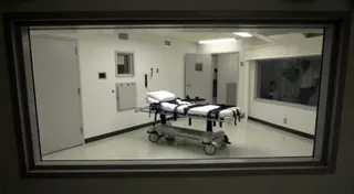 A white padded gurney with black restraint straps sits in Alabama's lethal injection chamber with a wheeled cart in the foreground