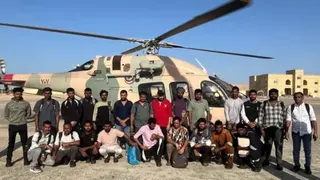A group of Indian seafarers pose in front of a helicopter.