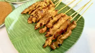 Chicken satay skewers on a green leaf-patterned plate